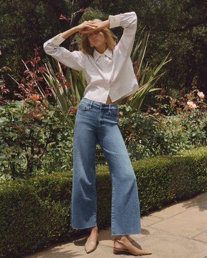Woman in a garden wearing a white blouse and blue flared jeans