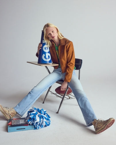 Blonde woman wearing a brown leather jacket and blue jeans sitting on a desk chair